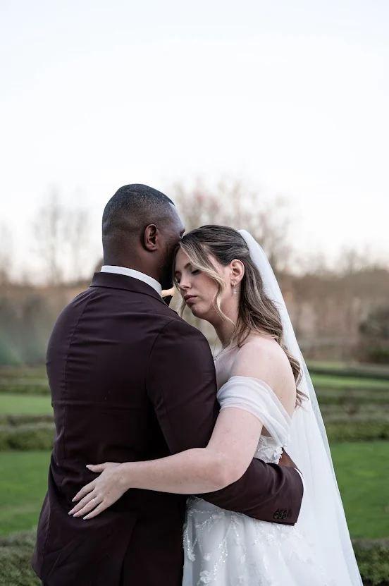 Les mariés enlacés dans un jardin à la française, la mariée les yeux fermés contre le front de son époux