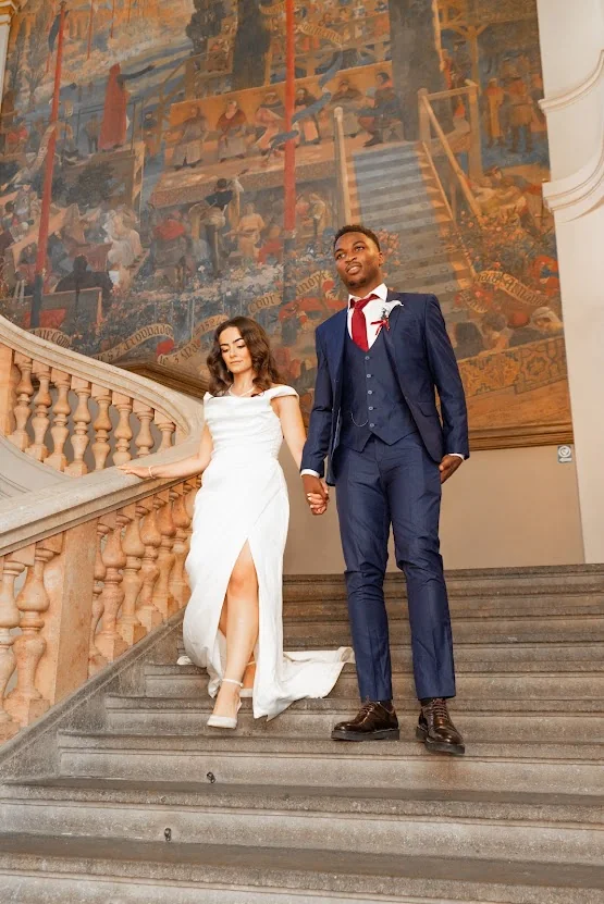 Les mariés descendant ensemble un grand escalier de pierre, devant une fresque monumentale