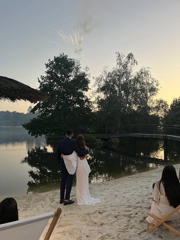Hortense et Zoheir enlacés au bord d’un lac au crépuscule, devant un feu d’artifice