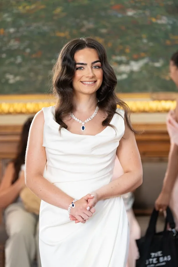Portrait de la mariée, sourire aux lèvres, collier de cristal et robe blanche drapée