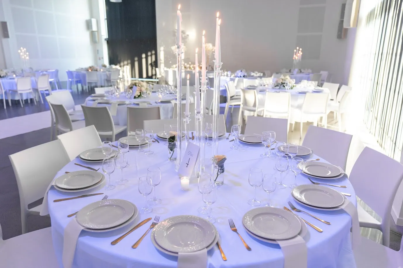 Une table ronde dressée dans la salle de réception : nappe blanche, chandeliers de cristal à bougies longues et verres alignés