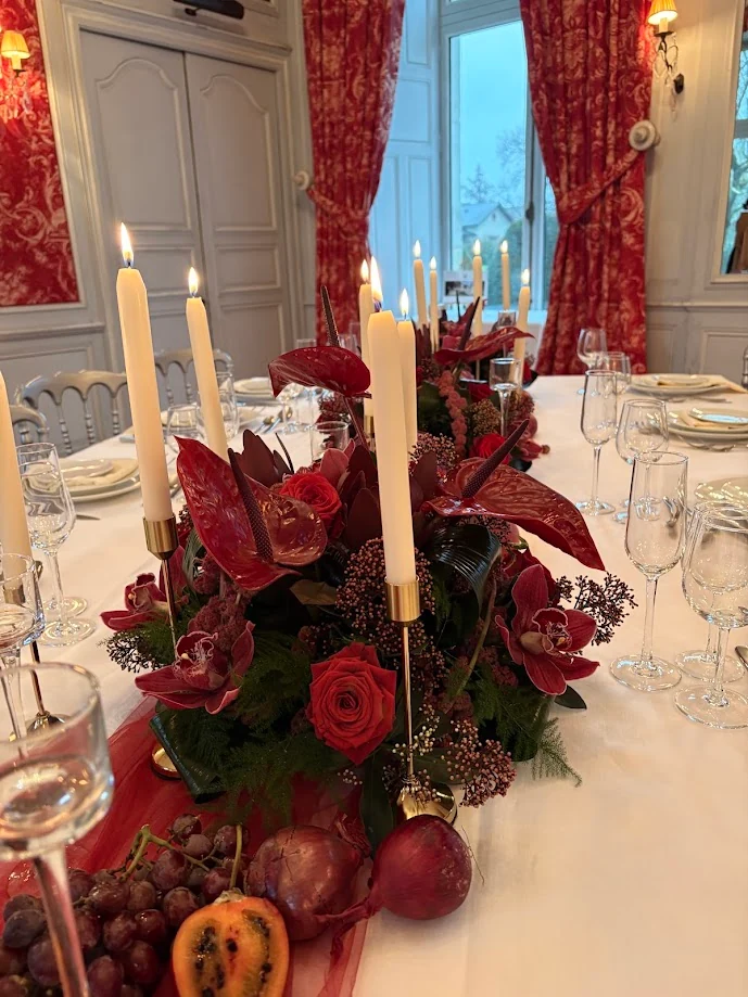 Table de salon de château aux rideaux de toile rouge : bougies allumées, centre de table d’anthuriums rouges, de roses et de fruits