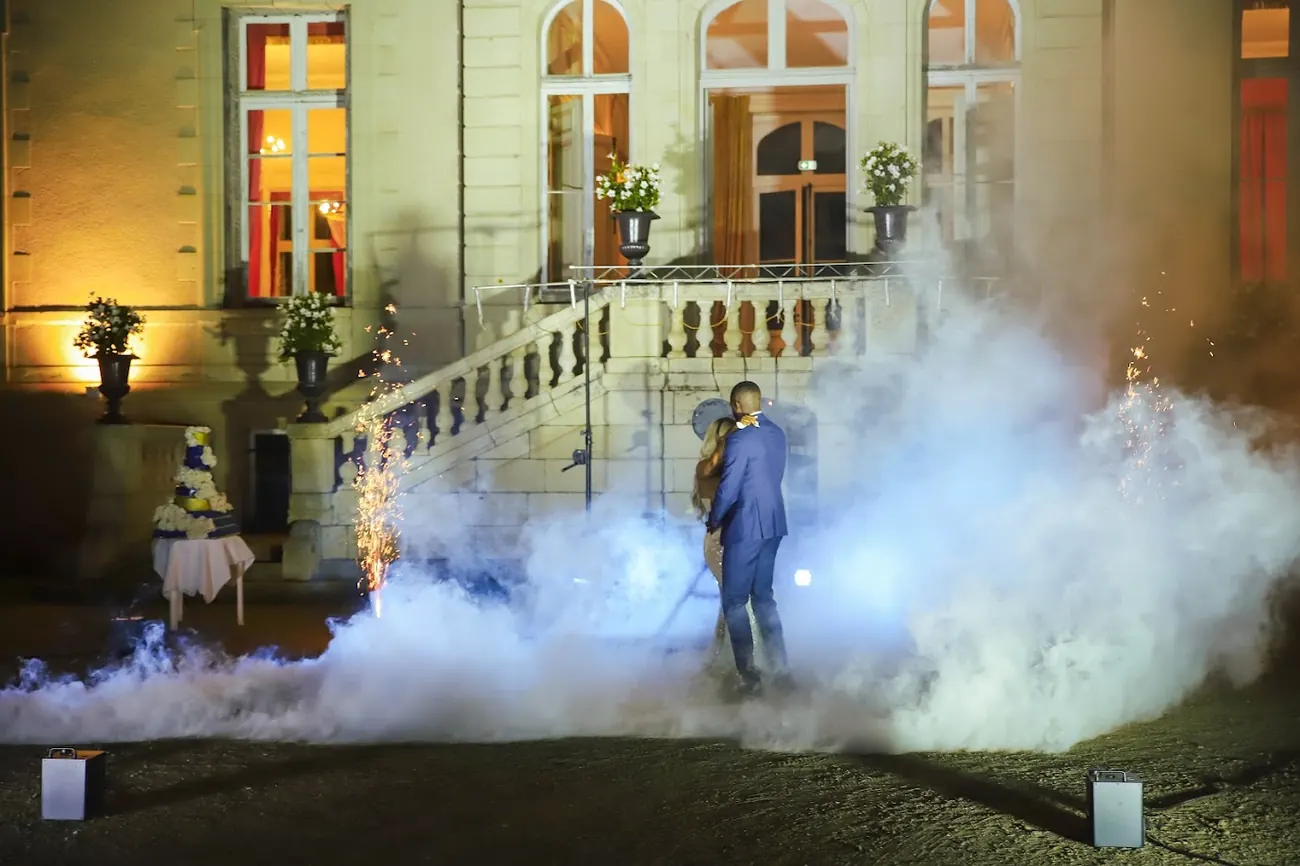 Au pied du perron d’un château illuminé, les mariés dansent enlacés dans la fumée et les étincelles, à côté de leur pièce montée