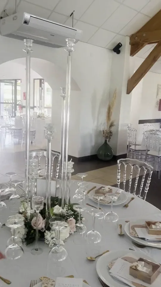 Film : de hauts chandeliers de cristal et un centre de table de fleurs blanches, dans une salle aux arches blanches et aux chaises transparentes