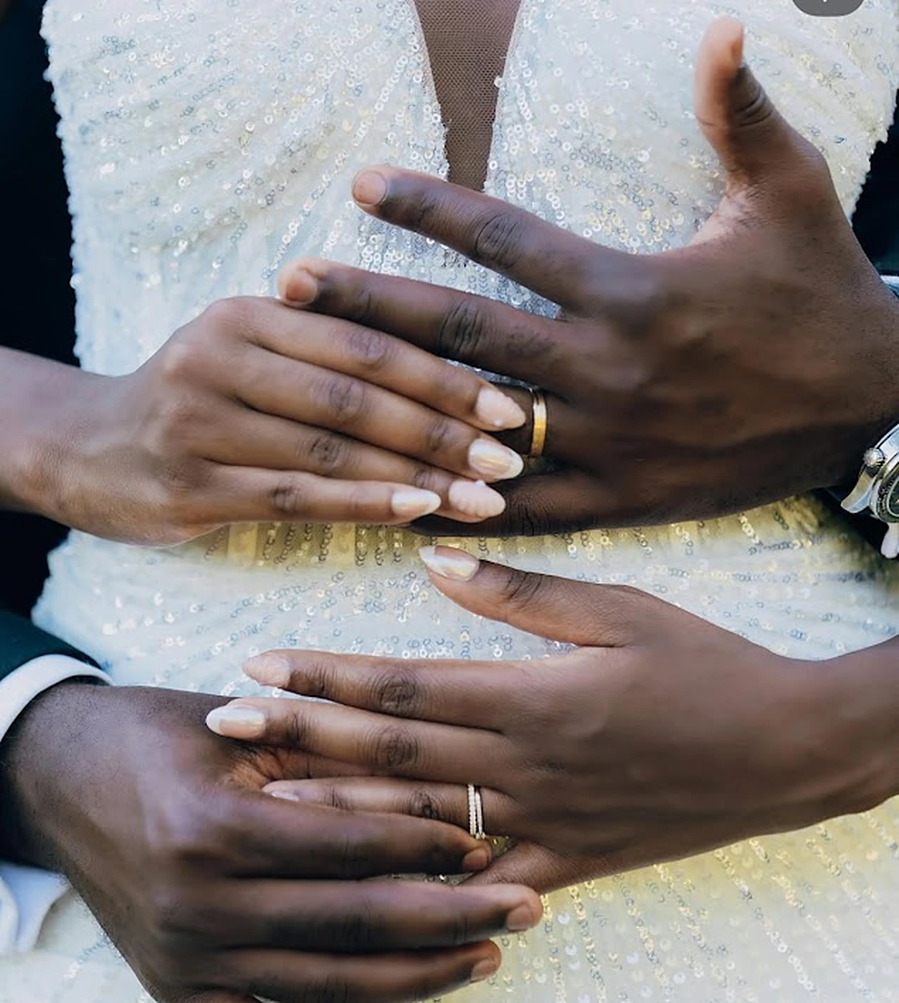Les mains des mariés enlacées sur la robe de sequins, alliances visibles