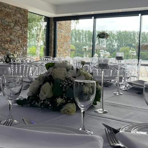 Détail d’un centre de table : roses blanches, marguerites et gypsophile, verres et serviettes en premier plan