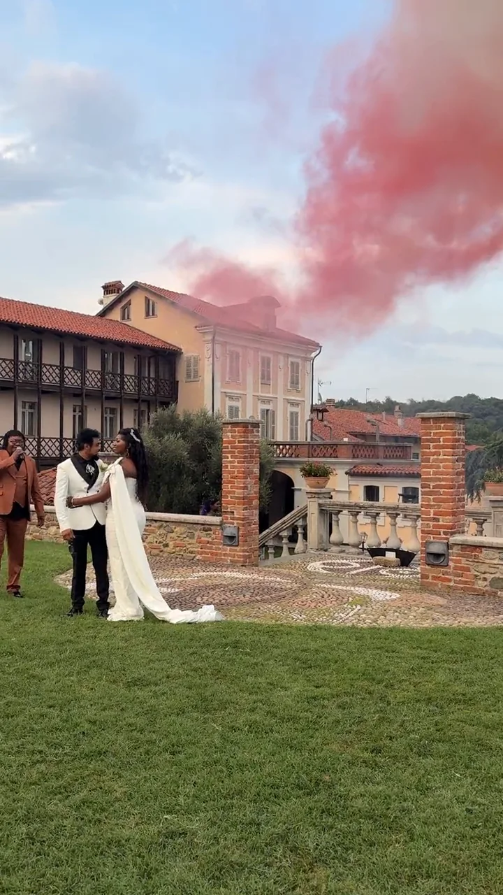 Film : les mariés enlacés dans les jardins de la Villa Merlin, avec les toits de tuiles de la villa et un nuage de fumée colorée dans le ciel