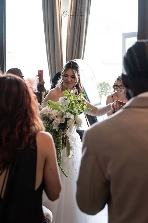 Marine entre dans la salle, son bouquet de fleurs blanches et vertes à la main, au milieu des invités