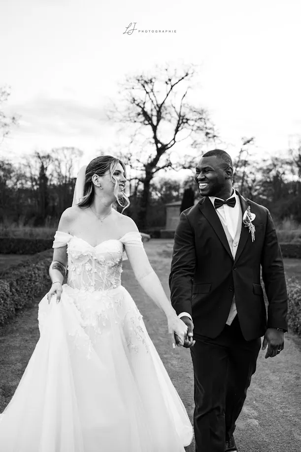 En noir et blanc, Marine et Yacouba, main dans la main, éclatent de rire dans une allée du jardin