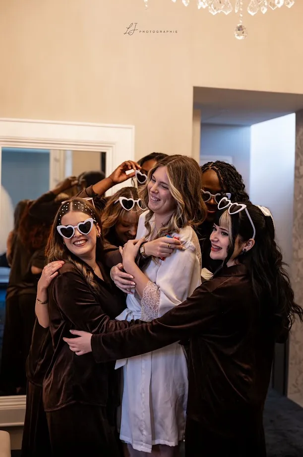 Dans une chambre, la mariée en peignoir blanc entourée de ses demoiselles d’honneur en velours brun, toutes en lunettes cœur