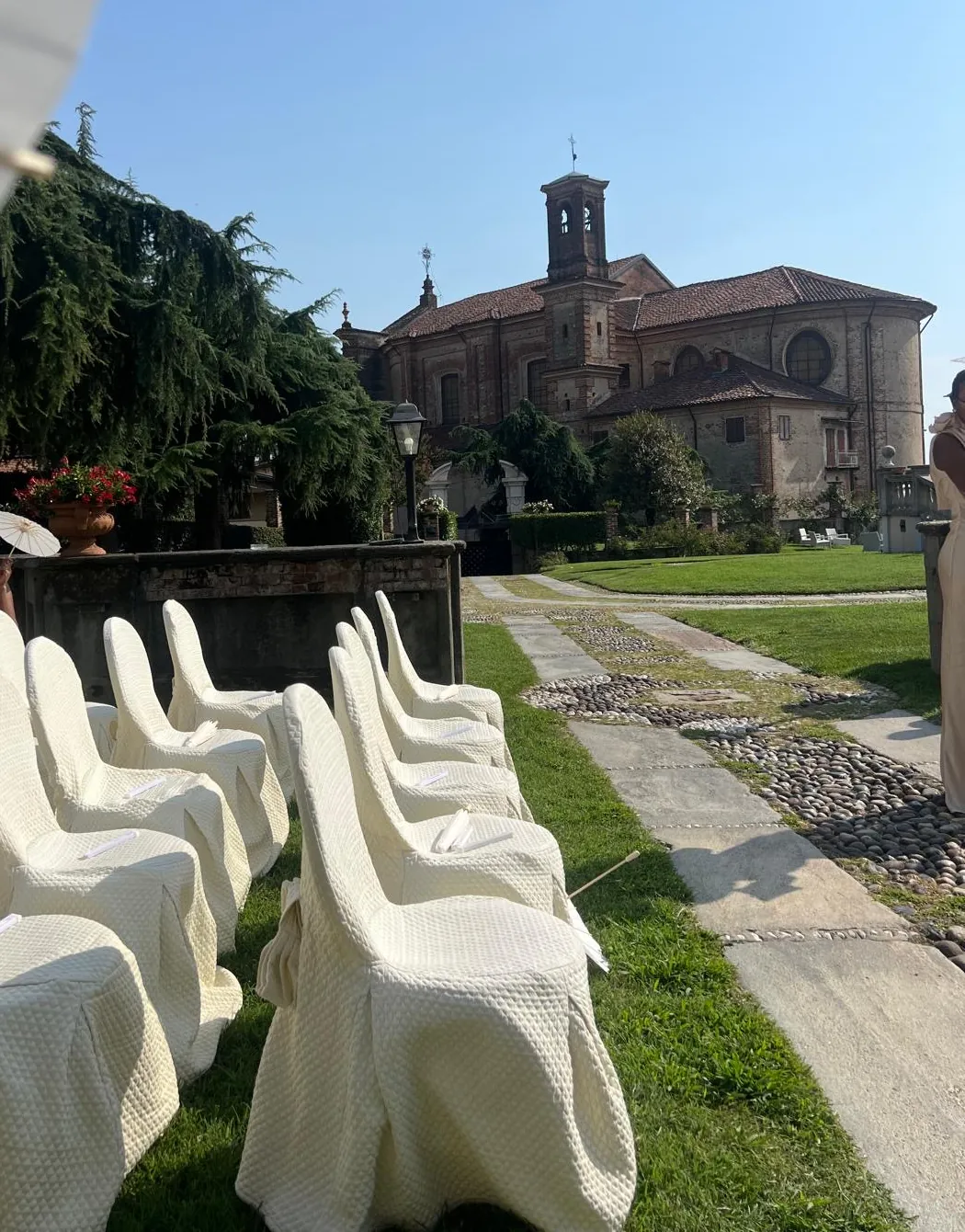 Cérémonie en plein air à la Villa Merlin : rangées de chaises habillées de blanc sur la pelouse, face à l’église, sous un ciel bleu