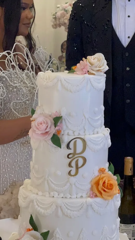 Détail de la pièce montée : trois étages de crème, fleurs roses et orangées et le monogramme P & D doré